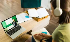 Dziewczyna w słuchawkach uczy się w domu. Na ekranie laptopa widać nauczycielkę prowadzącą lekcję w ramach polskiej szkoły internetowej.