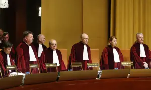 Siedmiu sędziów w togach, w tym jedna kobieta, stoi w sali sądowej. Wszyscy mają na sobie białe żaboty. W tle widać złote zasłony.