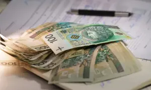 Stos banknotów 100 zł na dokumentach, symbolizujący niską emeryturę w Polsce.