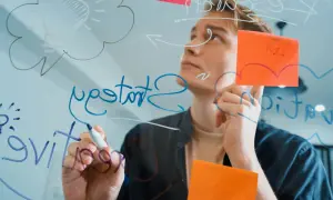 Młody mężczyzna pisze na szkle, tworząc schemat myśli i notując pomysły. To wizualizacja tego, jak uczyć się efektywnie.