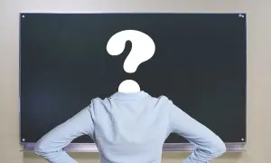 Nauczyciel z pytajnikiem zamiast głowy przed tablicą. Czy to symbol problemów z godzinami ponadwymiarowymi nauczycieli?