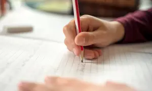 Dłoń pisze ołówkiem po zeszycie w linie. Dziecko z orzeczeniem o dysortografii ćwiczy pisanie, by pokonać trudności.
