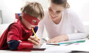 Chłopiec w stroju superbohatera rysuje, a mama z uśmiechem wspiera go, pokazując, jak zachęcić dziecko do nauki przez zabawę.