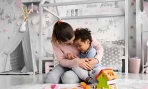 Ciepła opieka na dziecko w pokoju pełnym zabawek. Matka tuli synka, otoczeni klockami i namiotem tipi.