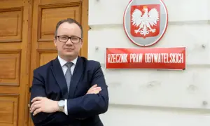 Mężczyzna w garniturze stoi przed budynkiem z godłem Polski i tabliczką "Rzecznik Praw Obywatelskich".