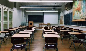 Pusta sala lekcyjna z rzędami ławek i krzeseł, tablicą, mapą świata i ekranem projekcyjnym. Idealne miejsce do nauki w branżowej szkole 2 stopnia.