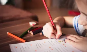 Dziecko pisze, być może przygotowując się do wydania orzeczenia z poradni psychologiczno-pedagogicznej. Kolorowe kredki leżą obok.
