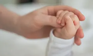 Dłoń rodzica obejmuje maleńką dłoń dziecka. To symbol miłości i wsparcia, a także świadczenie rodzicielskie.