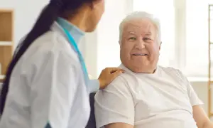 Uśmiechnięty starszy pan otrzymuje wsparcie od pielęgniarki. To przykład troski i świadczenia pielęgnacyjnego.