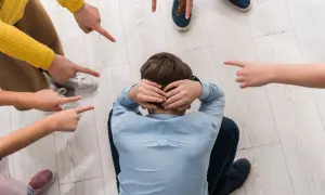 Chłopiec skulony na podłodze, otoczony przez palce wskazujące na niego. To obraz tego, co to jest bullying w szkole.