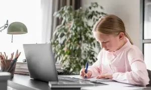 Dziewczynka uczy się w domu, pisząc notatki. Zastanawia się, ile kosztuje nauczanie domowe, analizując materiały na laptopie.