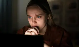 Zmartwiona dziewczyna z niebieskimi oczami patrzy na ekran komputera, przeżywając **zastraszanie** w sieci.