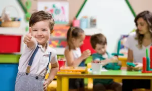 Uśmiechnięty chłopiec pokazuje kciuk w górę w przedszkolu, gdzie od kiedy zerówka jest obowiązkowa, dzieci bawią się i uczą.