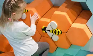 Dziewczynka dotyka dekoracji w kształcie plastra miodu z pszczołami.