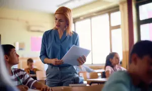 Nauczyciel początkujący z zeszytem w ręku rozmawia z uczniem w klasie.