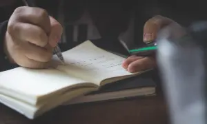 Dłoń pisze w zeszycie, przygotowując opinię z poradni psychologiczno-pedagogicznej.