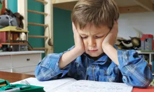 Chłopiec z problemem z koncentracją u dziecka, z rękami na uszach, siedzi przy biurku, próbując odrobić lekcje.
