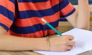 Dziecko z bransoletką pisze ołówkiem. Trudności z pisaniem mogą być oznaką, co to jest dysgrafia.