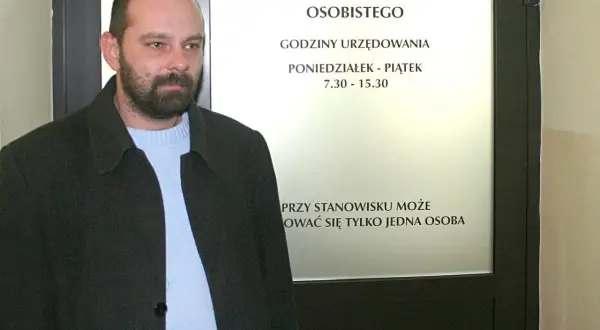 Mężczyzna czeka na informację, ile kosztuje wyrobienie dowodu osobistego. Tablica informuje o godzinach urzędowania.