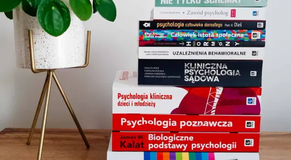Stos książek o psychologii, w tym psychologia kliniczna, obok rośliny w doniczce.