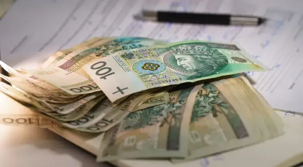 Stos banknotów 100 zł na dokumentach, symbolizujący niską emeryturę w Polsce.