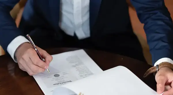 Mężczyzna w garniturze podpisuje dokument, składając oświadczenie woli.
