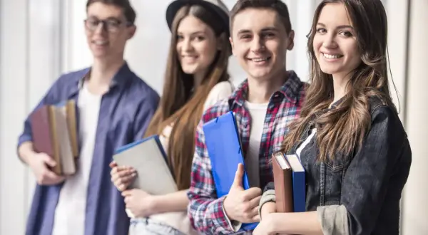 Uśmiechnięci młodzi ludzie z książkami i teczkami. Czy szkoła policealna daje status studenta?