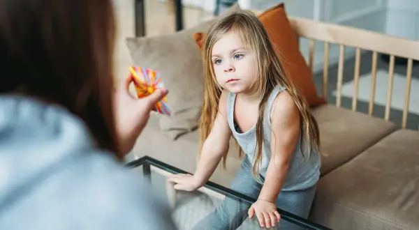 Dziewczynka z uwagą patrzy na kolorową zabawkę trzymaną przez mamę. Czy afazja u dzieci jest wyleczalna? Terapia może pomóc.
