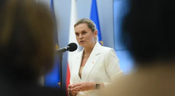 Minister edukacji przemawia przy mikrofonie, w tle flagi Polski i UE.