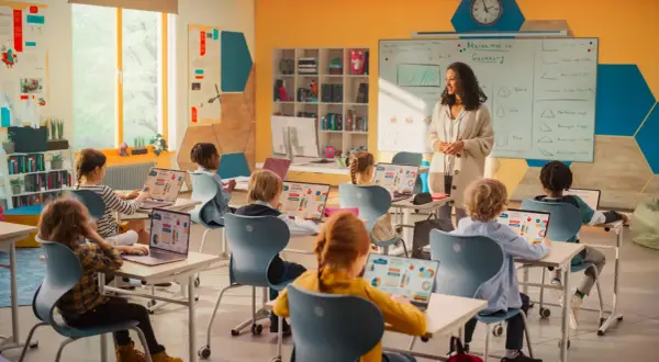 Nauczycielka prowadzi lekcję matematyki w nowoczesnej klasie. Dzieci uczą się z laptopów, co pokazuje postęp w pracy w oświacie.