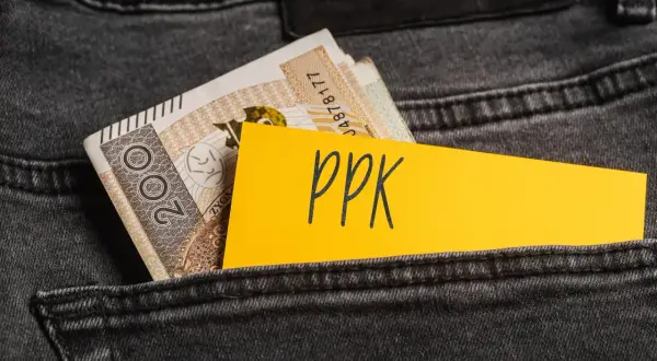 Żółta kartka z napisem "ppk" wystaje z kieszeni dżinsów obok banknotów. Decyzja o rezygnacji z PPK.