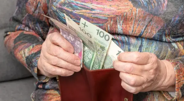Dłonie starszej osoby wkładają polskie banknoty do portfela. Zastanawiasz się, o ile wzrośnie emerytura po roku pracy na emeryturze?