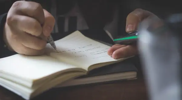 Dłoń pisze w zeszycie, przygotowując opinię z poradni psychologiczno-pedagogicznej.