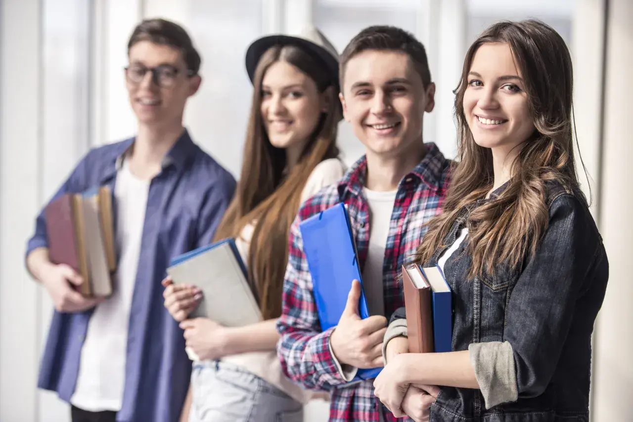 Uśmiechnięci młodzi ludzie z książkami i teczkami. Czy szkoła policealna daje status studenta?
