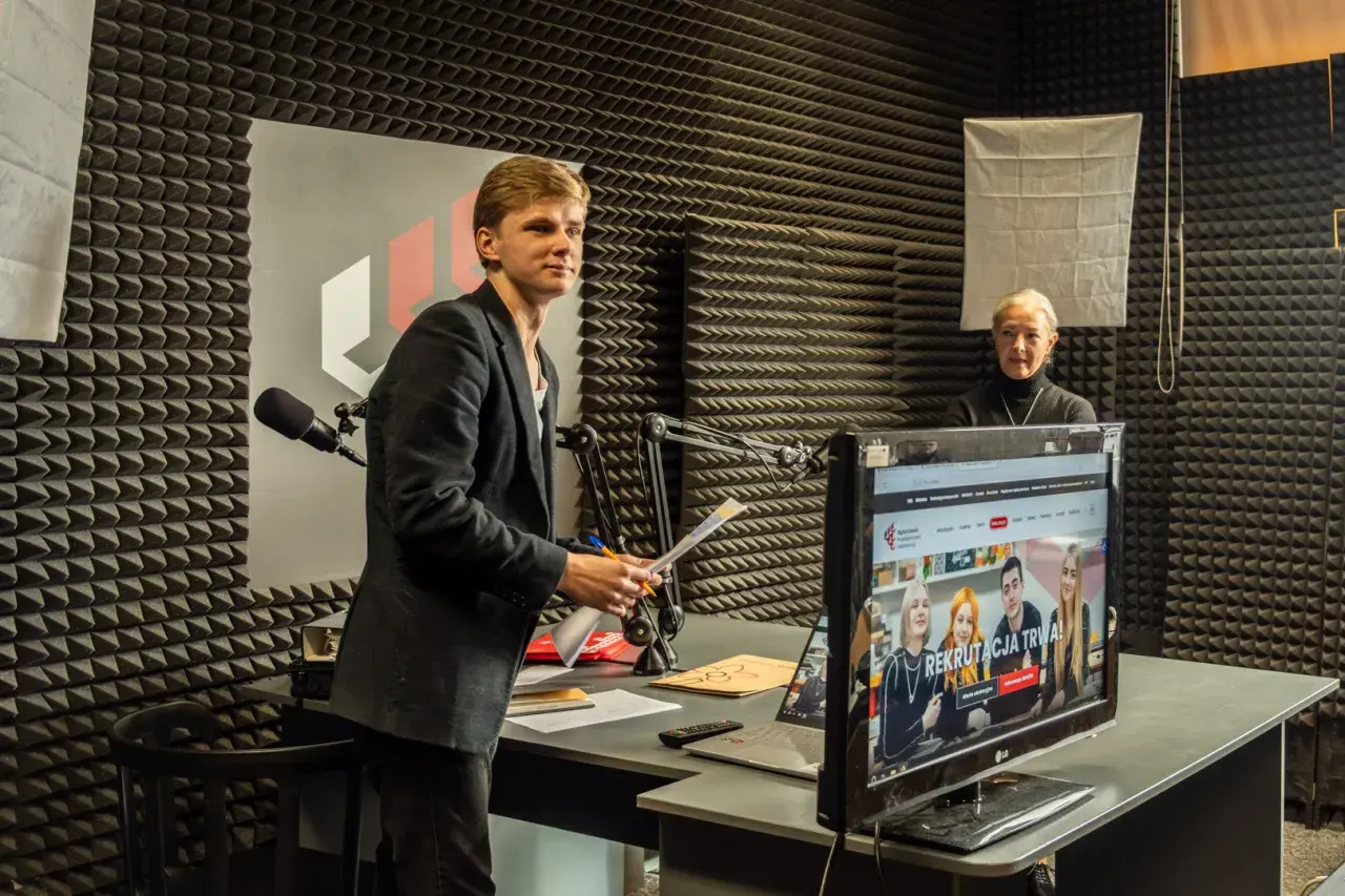 Młody mężczyzna z dokumentami w ręku i starsza kobieta w studiu radiowym. Rozmawiają o tym, czy po technikum można iść na studia.