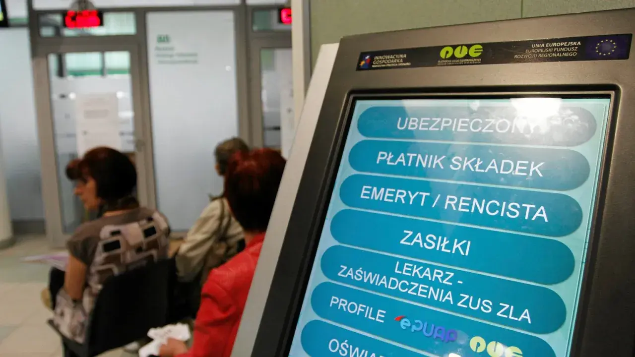 Terminal samoobsługowy w urzędzie, gdzie można uzyskać m.in. zaświadczenie o niezaleganiu ZUS. W tle czekający ludzie.