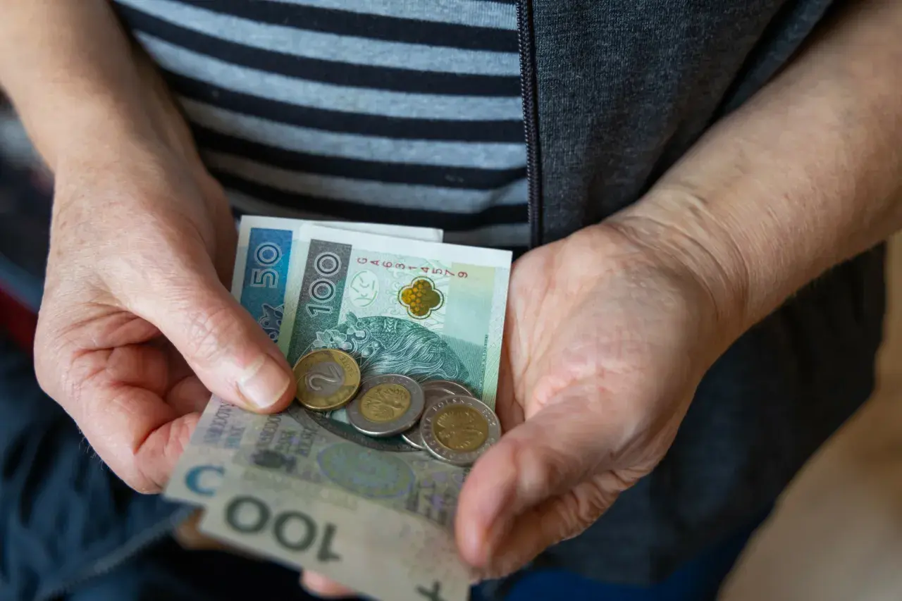 Dłonie trzymają polskie banknoty i monety. Nadzieja na waloryzację rent i emerytur 2026.