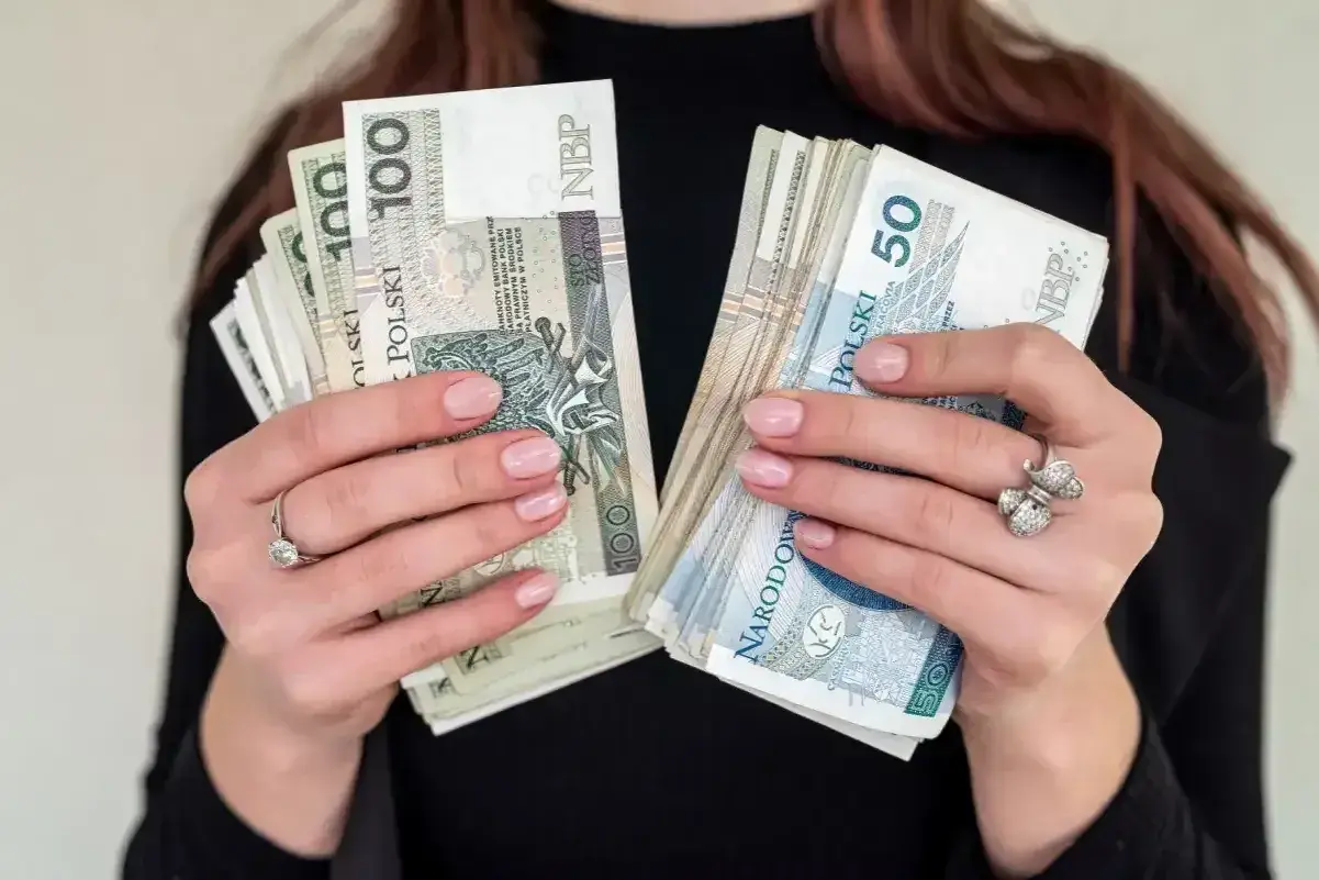 Dłonie trzymające pliki polskich banknotów 100 i 50 zł. Zastanawiasz się, jaka emerytura przy zarobkach 7000 brutto?