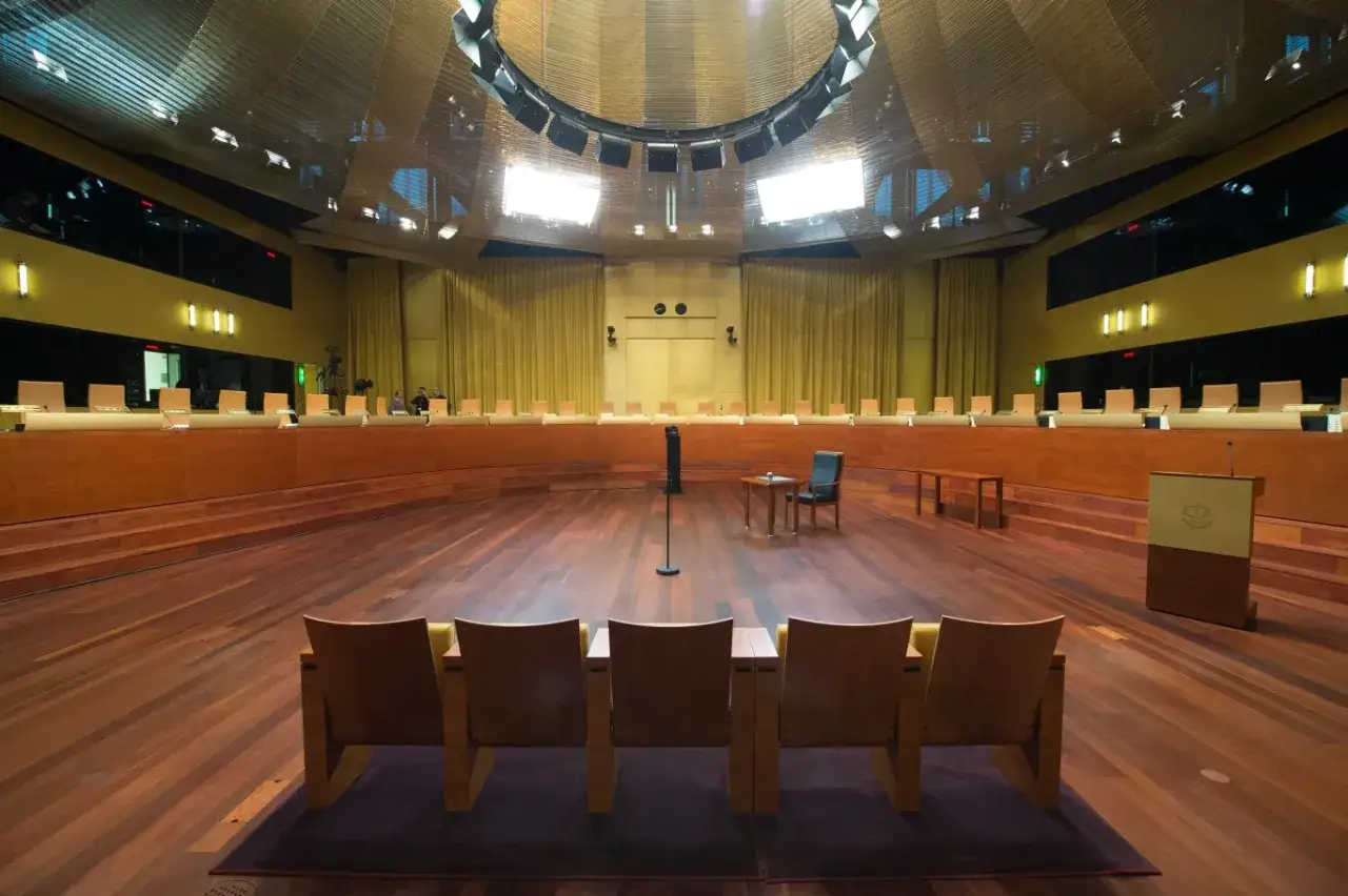 Pusta sala sądowa z drewnianą podłogą i półkolistym rzędem krzeseł. W centrum stoi mikrofon, a po prawej mównica. To miejsce, gdzie zapadają ważne tsue.