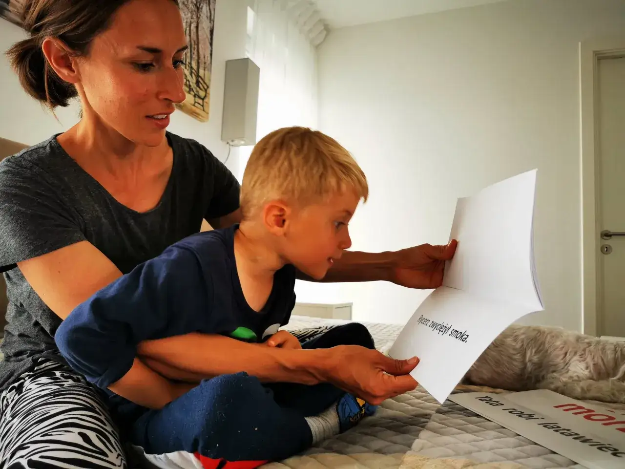 Mama pomaga synkowi, jak zacząć uczyć dziecko czytać, czytając mu książkę.