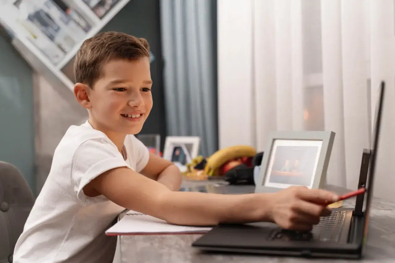 Uśmiechnięty chłopiec uczy się w polskiej szkole internetowej, wskazując palcem na ekran laptopa.