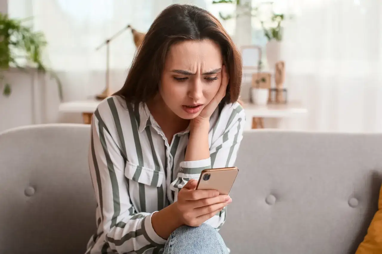 Zmartwiona kobieta siedzi na kanapie, trzymając telefon. Czyżby jej urlop na żądanie został odrzucony?
