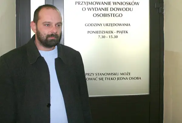 Mężczyzna czeka na informację, ile kosztuje wyrobienie dowodu osobistego. Tablica informuje o godzinach urzędowania.