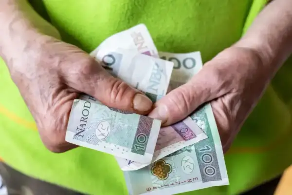 Dłonie trzymają polskie banknoty. Nowe zasady przyznawania renty socjalnej mogą wpłynąć na finanse wielu osób.