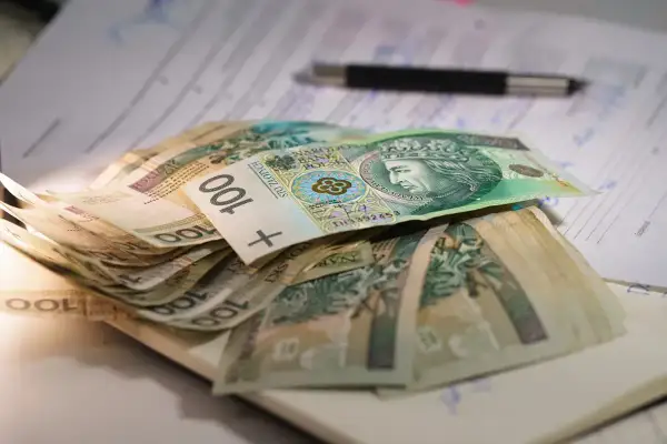Stos banknotów 100 zł na dokumentach, symbolizujący niską emeryturę w Polsce.