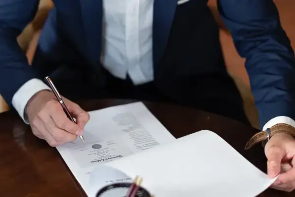 Mężczyzna w garniturze podpisuje dokument, składając oświadczenie woli.