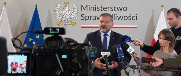 Minister sprawiedliwości przemawia do mediów, otoczony flagami Polski i UE. Dziennikarze zbierają materiał do reportażu o wyroku TSUE.