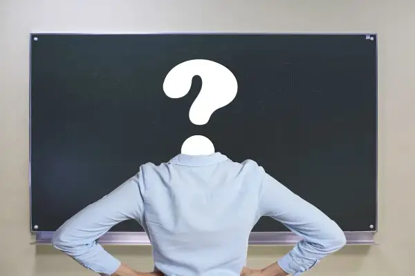 Nauczyciel z pytajnikiem zamiast głowy przed tablicą. Czy to symbol problemów z godzinami ponadwymiarowymi nauczycieli?