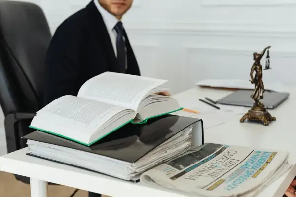 Prawnik w garniturze studiuje prawo, obok otwarty kodeks, akta i Dziennik Gazeta Prawna. Czas na vacatio legis.