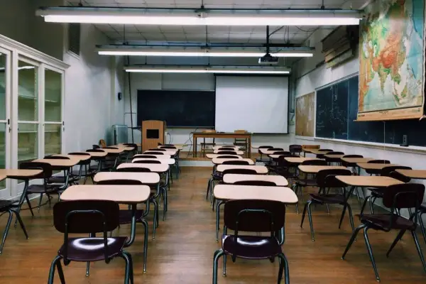 Pusta sala lekcyjna z rzędami ławek i krzeseł, tablicą, mapą świata i ekranem projekcyjnym. Idealne miejsce do nauki w branżowej szkole 2 stopnia.